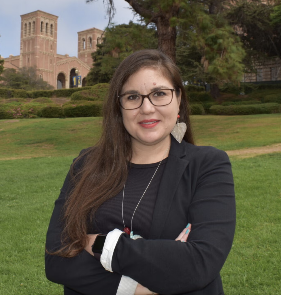Cynthia Salazar smiling outdoors in a black blazer and glasses, with green lawn and Royce Hall behind her.